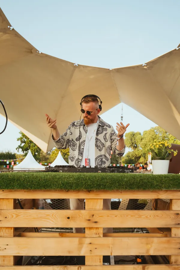Dawid an der DJ Booth unter einem Sonnensegel, die Booth aus Paletten